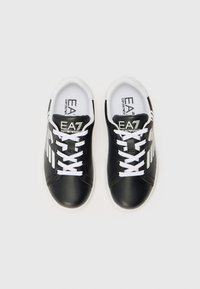 Baskets en cuir noir avec des lacets blancs, présentant un logo et des rayures sur les côtés. Bout arrondi et collier rembourré pour le confort.