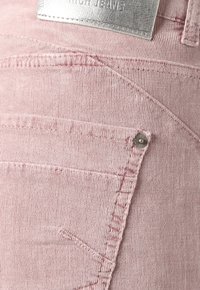 Růžové manšestrové džíny s vertikálním žebrováním, se zadní kapsou a stříbrnou kovovou nášivkou. Výrazné švy po celém povrchu.