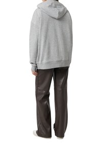 Szara bluza z kapturem o luźnym kroju, z prążkowanymi mankietami i kieszenią kangurką. Połączona z brązowymi skórzanymi spodniami i białymi trampkami.