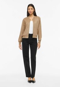 Pruun bomberjakk made nahasarnast materjalist, ees tõmblukk, soonilised varrukaotsad ja vaba lõige. Sobitatud mustade sirgete säärtega pükstega.