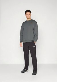 Felpa grigia texturizzata con collo rotondo e logo, abbinata a pantaloni neri con il nome del marchio. Entrambi hanno una vestibilità comoda.