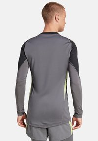 T-shirt de sport �à manches longues en gris avec des accents noirs et vert néon ; fabriqué en tissu lisse et extensible ; présente un col rond et une coupe ajustée.