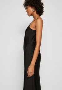 Robe en satin noir au design épuré, avec de fines bretelles et une texture lisse, mettant en valeur une silhouette de côté et une forme ajustée.