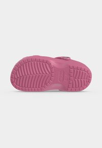Απλή όψη ροζ clog slip-on με υφή στο πέλμα και στρογγυλό κουμπί στον ιμάντα σε λευκό φόντο.