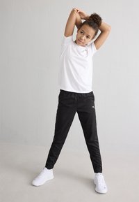 Maglietta sportiva bianca a maniche corte abbinata a pantaloni neri attillati e sneakers bianche. Design semplice, materiale leggero e vita elasticizzata.