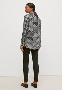 Long-sleeve, black and white patterned blouse with a high collar, paired with black slim-fit pants, viewed from the back. Flat shoes visible.