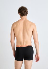Black boxer briefs with an orange waistband. The fabric appears smooth and fitted, showcasing a back view of the garment.