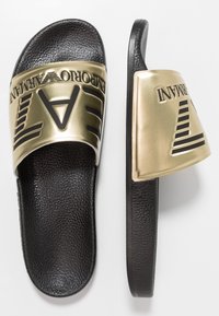 Czarne klapki z szerokim złotym paskiem z wytłoczonym czarnym napisem i geometrycznymi wzorami. Teksturowana wkładka dla komfortu.