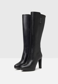 Bottes en cuir noir montantes avec une finition lisse, bout rond et un talon haut et épais. Présente un minimum de coutures et un accent de logo.