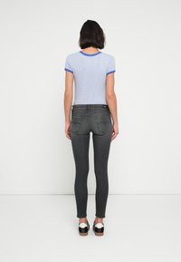 Light blue and white striped short-sleeve shirt with blue trim paired with dark gray fitted jeans and black shoes with a white accent.