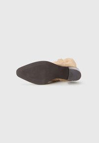 Bottine en suède de couleur beige avec une texture lisse, dotée d'une semelle en caoutchouc noire et d'un design à bout rond.