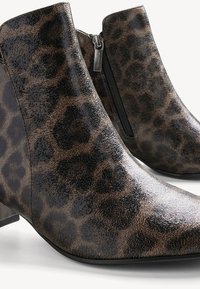 Bottines montant à la cheville avec motif léopard marron foncé et noir, surface texturée et fermeture éclair latérale.