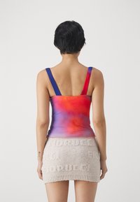 Top a canotta multicolore con una sfumatura dal rosso al viola, con spalline larghe e design senza cuciture, abbinato a una minigonna beige testurizzata.