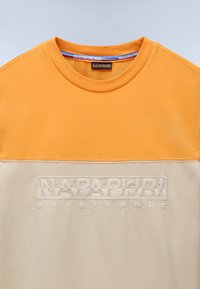 Kortærmet t-shirt med en orange øvre sektion og en lys beige nederste sektion, der har et broderet logo i midten. 100% bomuldsstof.