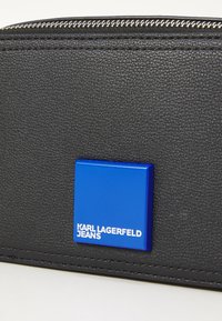 Black textured wallet featuring a blue rectangular logo plate with "KARL LAGERFELD JEANS" in white, and a silver zipper.