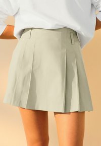 Jupe plissée vert clair en tissu texturé, avec une taille haute et des poches latérales. Design simple avec une apparence propre et ajustée.