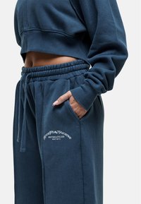 Afgebroken marineblauwe sweatshirt met een ontspannen pasvorm en geribde manchetten, gecombineerd met bijpassende joggingbroek met elastische taille en logo-detail.