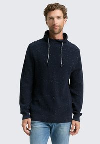 Marineblauer Strickpullover mit gesprenkelter Textur, Trichterkragen, grauen Kordelzügen und langen Ärmeln. Trägt man zu einer hellen Jeans.