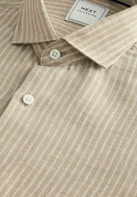 Beige striped shirt with a textured fabric, featuring a fold-down collar and two white buttons at the placket. Label reads "NEXT TAILORING."
