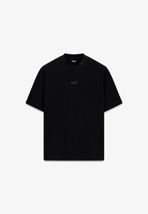 T-shirt noir en coton avec un col rond et des manches courtes. Présente un logo "GUESS" discret dans une teinte légèrement plus foncée sur le devant.