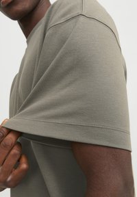 Olivengrønt t-shirt med kortærmer lavet af blødt stof med synlige sømdetaljer, en afslappet pasform og en justerbar kant.