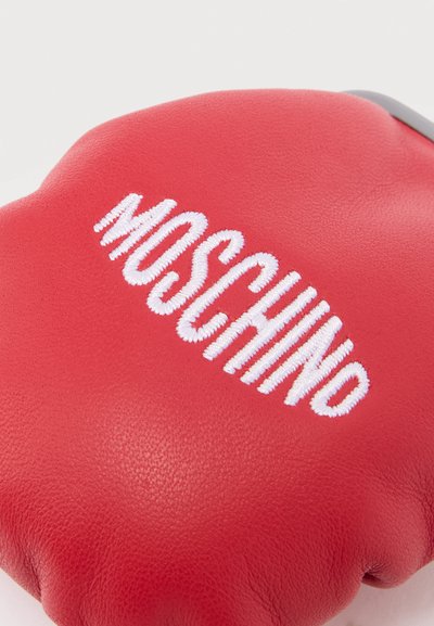 Κόκκινο δερμάτινο γάντι πυγμαχίας με λευκό κεντημένο λογότυπο "MOSCHINO" στην επάνω επιφάνεια.