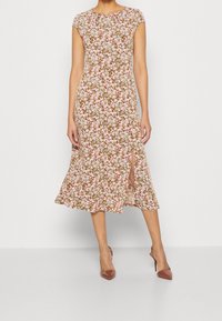 Robe midi florale aux tons rose clair et vert. Elle présente des manches courtes, un col rond et une fente latérale. Tissu doux et léger avec un ourlet fluide.
