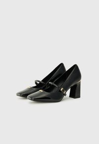 Black patent leather Mary Jane heels featuring a pointed toe, block heel, and adjustable strap with a gold buckle detail.