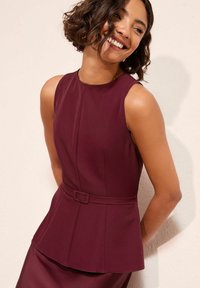 Bordó ujjatlan ruha, testre szabott felsőrésszel, peplum derekú és öv részlettel. Sima anyag enyhe fényes csillogással.