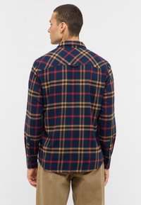 Langarm geruite shirt in marineblauw, tan en rood; met knopenmanchetten, een puntige kraag en een rugpand. Zacht textiel met een warme textuur.