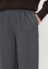 Graue Hose aus einem glatten, leichten Stoff, mit elastischem Bund und Seitentaschen, maßgeschneidert mit leichten Falten für eine lockere Passform.