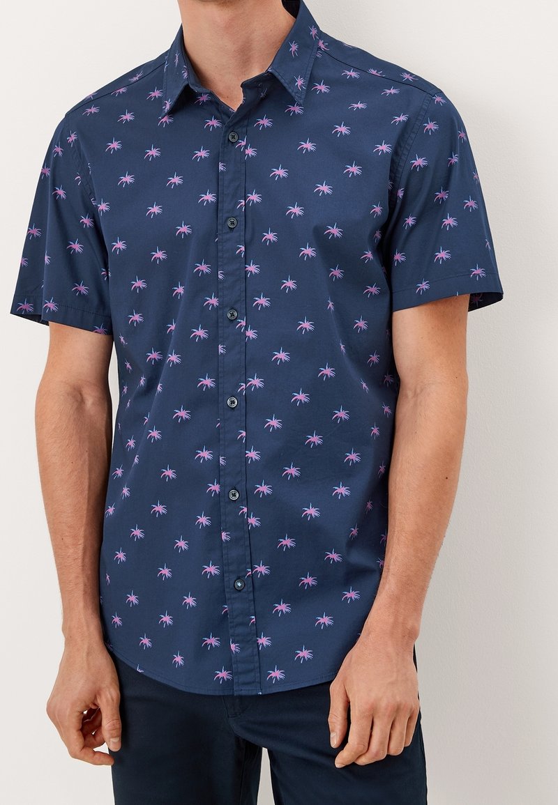 Homme portant une chemise bleu marine à manches courtes avec un motif d'araignée rose.