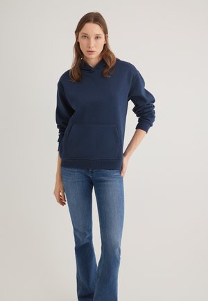 Navyblauer Hoodie aus weichem Baumwollmaterial, mit einer Fronttasche, einer Kapuze mit Kordelzug und gerippten Bündchen, kombiniert mit hellblauen Schlagjeans.