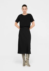 Fekete midi ruha rövid ujjakkal, kerek nyakkivágással, meghúzott derékkal és sima textúrával, mintás térdig érő csizmával párosítva.