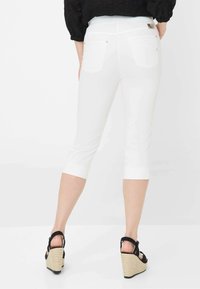Pantaloni capri bianchi realizzati in tessuto misto cotone, con vita a media altezza, orli risvoltabili e tasche posteriori con dettaglio logo.