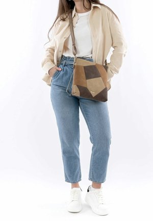 Mujer con chaqueta beige, camisa blanca, vaqueros azules de cintura alta, zapatillas blancas y un bolso cruzado marrón de patchwork.