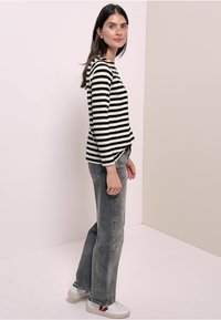 Schwarz-weiß gestreiftes Langarmoberteil kombiniert mit grauen weit geschnittenen Jeans und weißen Turnschuhen. Einfaches Design mit lässigem Schnitt und strukturiertem Stoff.