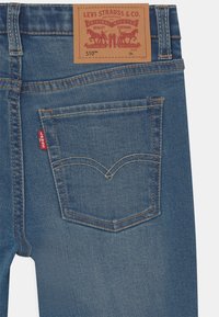 Jeans de mezclilla de color azul oscuro con una etiqueta de cuero de la marca "Levi Strauss & Co." que cuenta con un pequeño rectángulo rojo en el bolsillo trasero y costuras de doble puntada.
