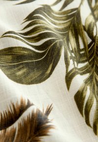 Tissu présentant un imprimé botanique avec des feuilles vertes et brunes sur un fond crème clair, doté d'une surface douce et texturée.