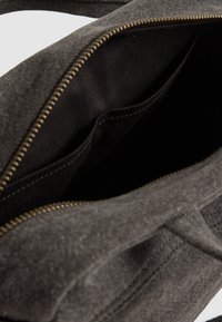 Grijze stoffen tas met een ritssluiting, met een gladde textuur en zwarte voering. Het interieur heeft twee vakken voor organisatie.