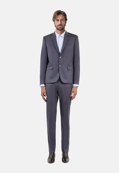 Traje gris a rayas con un corte ajustado, que presenta un blazer de dos botones y pantalones a juego, combinados con una camisa de vestir blanca y zapatos negros.