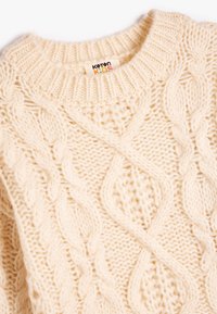 Cremfarbener gestrickter Pullover mit einem groben Kabelmuster, rundem Kragen und strukturiertem Stoff. Das Etikett trägt die Aufschrift "Koton Kids."