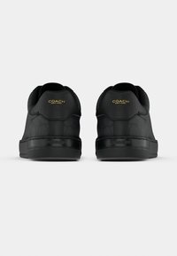 Schwarze Sneakers mit einer strukturierten Oberfläche, Gummisohle und gepolstertem Kragen. Goldene Logoakzente an Ferse und Seite.