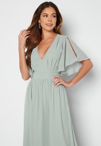 Hellgrünes, bodenlanges Kleid mit V-Ausschnitt und fließenden Ärmeln. Verfügt über eine taillierte Taille und weichen, plissierten Stoff. Keine sichtbaren Muster oder Akzente.