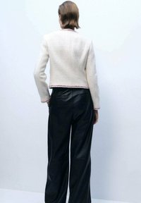 Witte textuurjacket met kleurrijke bies, gecombineerd met zwarte leren wijde broek. Het jacket heeft een rechte snit en geen zichtbare sluitingen.