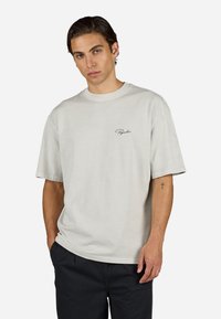 Lys grå bomulds t-shirt med rund hals, korte ærmer og et lille sort logo på brystet. Blød tekstur og afslappet pasform.