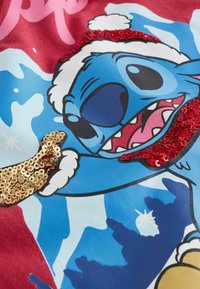 Tessuto rosso con un personaggio dei cartoni animati blu e un cappello bianco, impreziosito da paillettes rosse e dorate lucide, su uno sfondo azzurro chiaro.