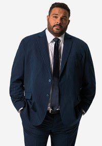 Marineblau gestreifter Anzugjacke mit zwei Knöpfen, einer einzigen Brusttasche; passende Hose; kombiniert mit einem weißen Hemd und einer dunklen Krawatte.