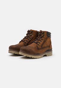 Botas de tobillo de cuero marrón con acabado texturizado, que cuentan con ojales de metal, cordones, un collar acolchado y una suela de goma resistente.