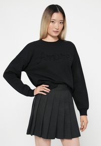 Felpa nera con la scritta "Amore" in dettagli di perline, abbinata a una mini gonna plissettata scura. Il tessuto sembra morbido, con un design a vestibilità rilassata.